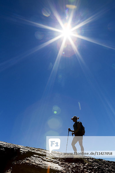 'Silhouette of female hiker on rocky ridge with blue sky and sunburst; Waterton  Alberta  Canada'