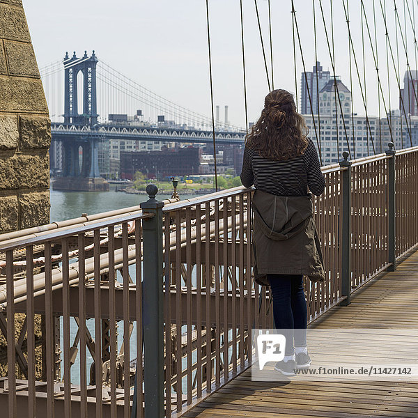 'A young woman stands on the Brooklyn Bridge looking out over the East River to the Manhattan Bridge; New York City  New York  United States of America'