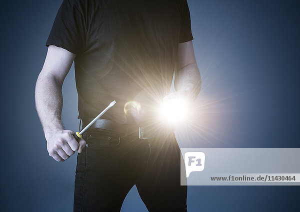Schwarz gekleideter Mann mit Taschenlampe und Schraubenzieher