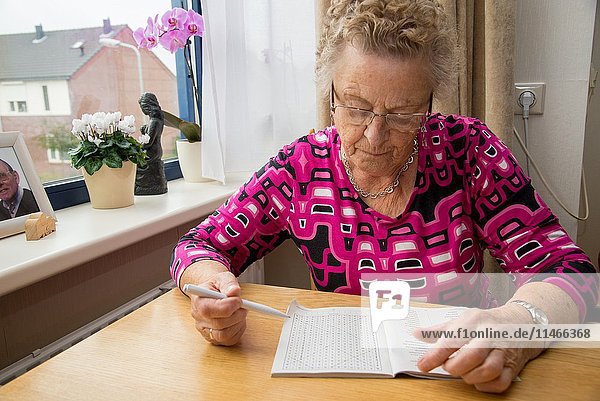Old woman makes wordpuzzle at table in home for the aged