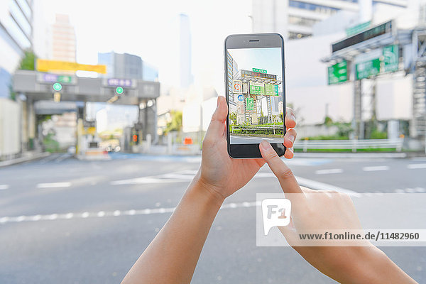 Japanische Frau  die eine Augumented-Reality-App auf ihrem Smartphone benutzt  in der Innenstadt von Tokio  Japan