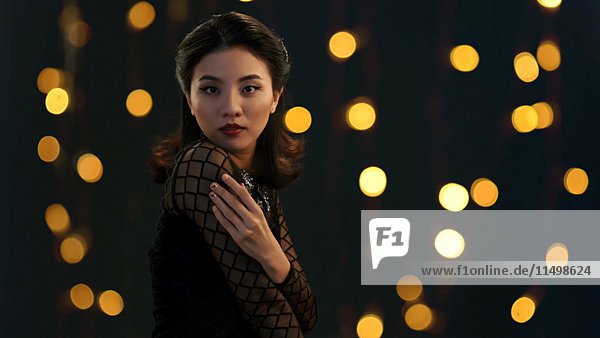 Taille-oben Porträt der jungen erwachsenen asiatischen Frau im schwarzen Kleid mit funkelnden Lichtern im Hintergrund
