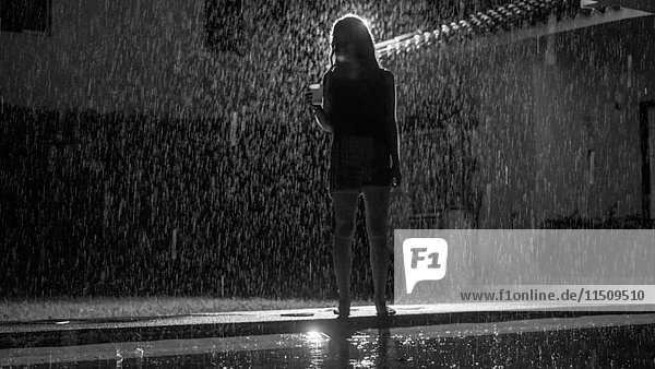 Junge erwachsene Frau  die nachts im Regen am Swimmingpool steht