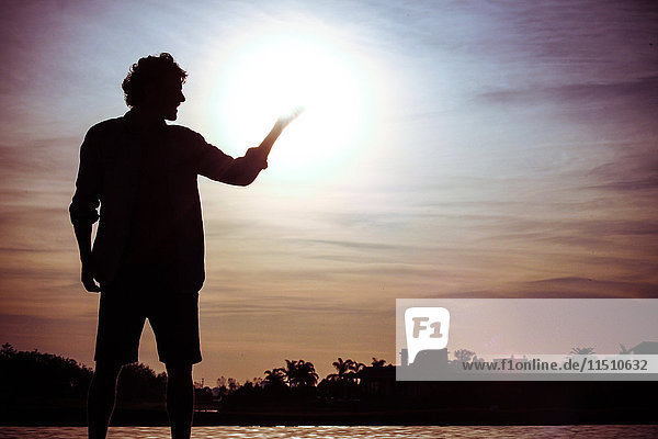 Man pretending to hold the sun at water's edge