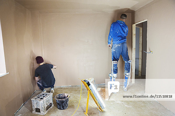 Ein Elektriker und Gipser  der an den Wänden eines im Bau befindlichen Hauses arbeitet.
