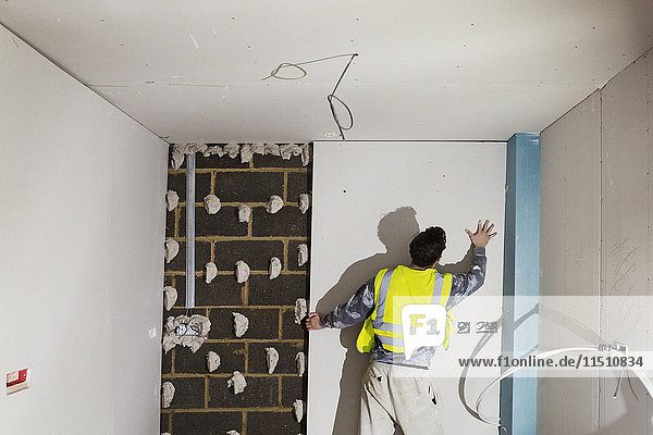 Ein Bauarbeiter  der Gipskartonplatten auf eine Wand aus Betonwerkstein montiert.