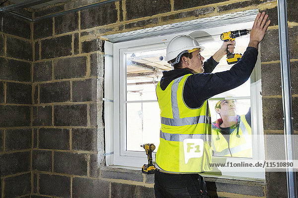 Ein Arbeiter auf einer Baustelle  ein Bauarbeiter mit Schutzhelm  der eine elektrische Bohrmaschine auf einem Fensterbrett benutzt.