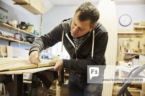 Mann  der in einer Holzwerkstatt am Rand eines Formbrettes aus Holz arbeitet.