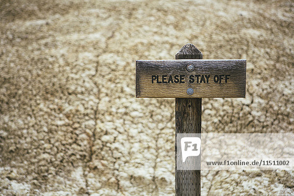 Gerissene,  ausgetrocknete Bodenoberfläche der Wüste und ein Please Stay Off-Schild auf der Oberfläche des Wüstensands.