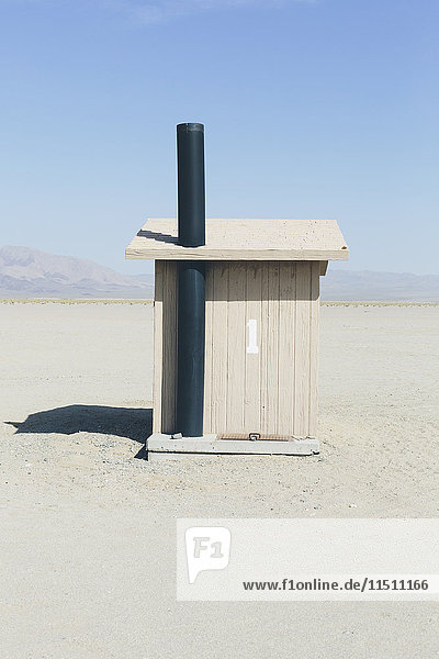 Toilette in einem offenen Raum,  einer Wüstenlandschaft. Weißer Sand und ein kleines Hüttengebäude.