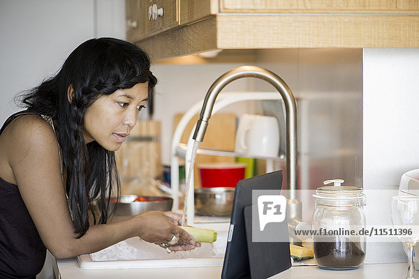 Frau benutzt digitale Tabletten bei der Zubereitung von Speisen zu Hause