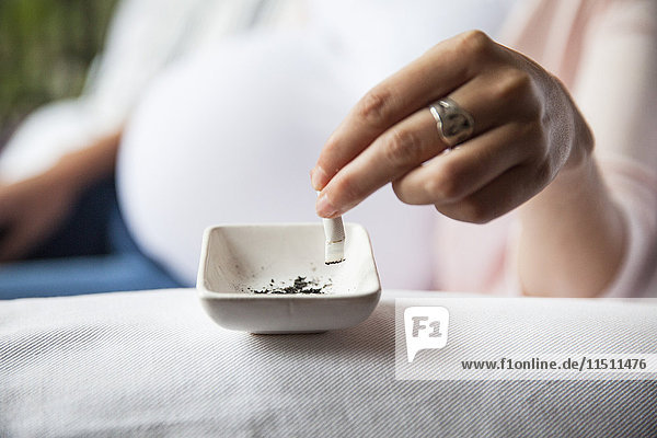 Pregnant woman putting cigarette out in ashtray