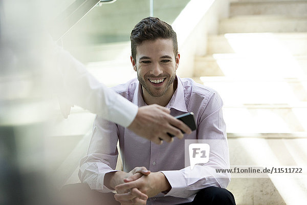 Businessman showing colleague content on smartphone