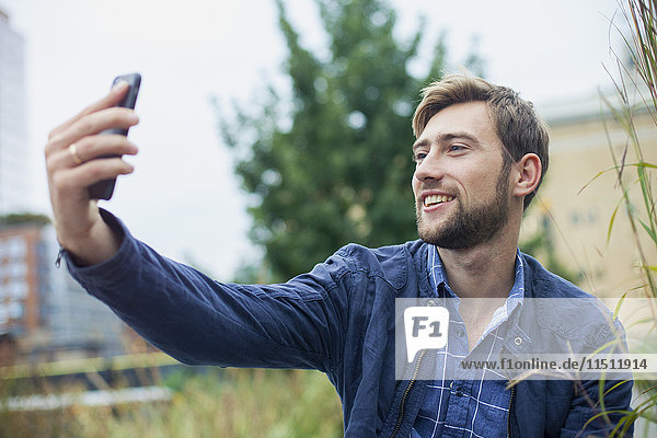 Junger Mann benutzt Smartphone um einen Selfie nach draußen zu bringen.