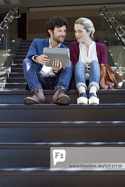 Paar auf Stufen sitzend  mit digitalem Tablett