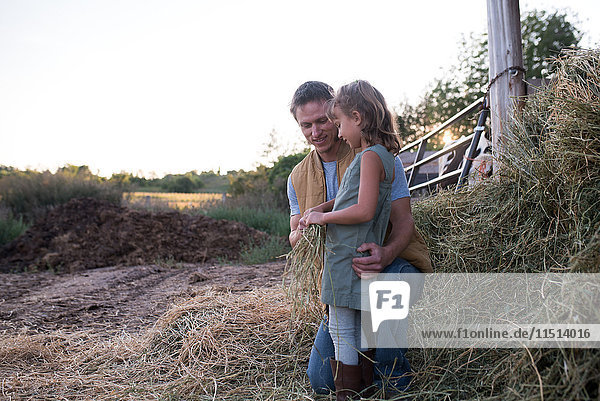 Vater und Tochter stehen zusammen auf dem Bauernhof  Tochter hält Heu