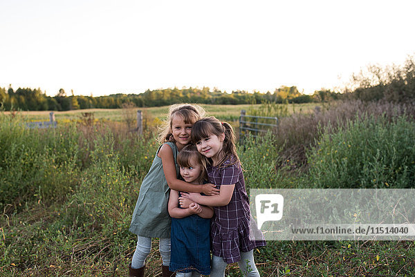 Porträt von drei jungen Mädchen  die zusammen im Feld stehen und sich umarmen
