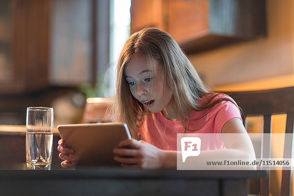 Junges Mädchen benutzt digitales Tablett am Küchentisch