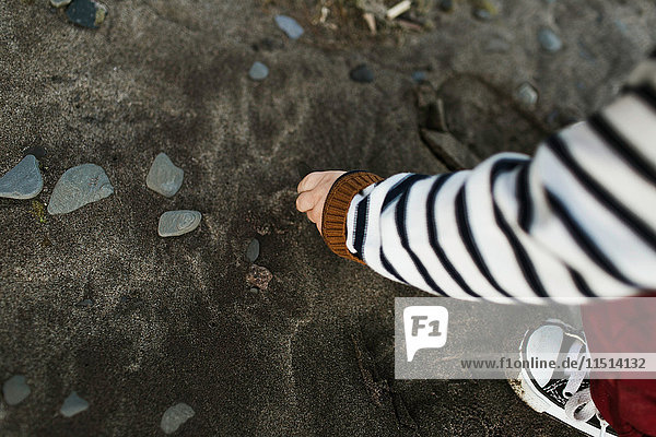 Geschnittene Ansicht eines kleinen Jungen am Strand  der Kieselsteine aufhebt