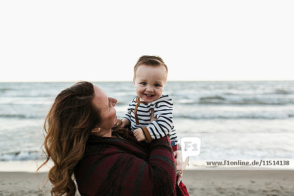Mutter am Strand hält lächelnden kleinen Jungen