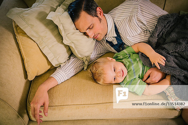 Vater und kleiner Sohn liegen zusammen auf dem Sofa