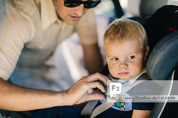 Father securing young son in car seat