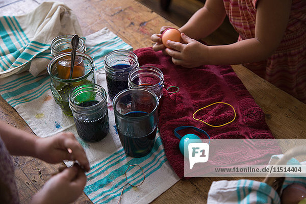 Hands of two young sisters dyeing easter eggs in jars at table