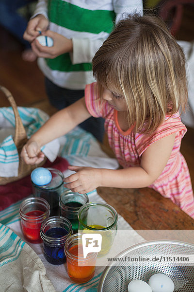 Girl and brother dyeing easter eggs in jars at table