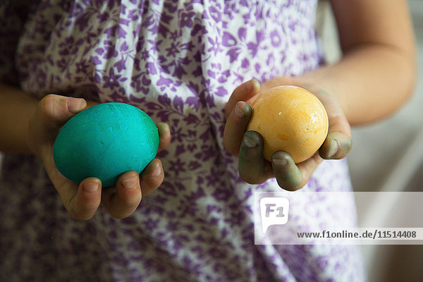 Mid section of girl holding blue and yellow dyed easter eggs