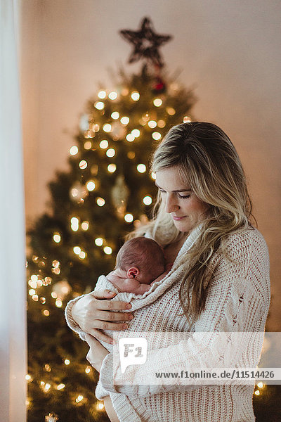 Mid adult woman cradling new born baby daughter wrapped in cardigan at Christmas