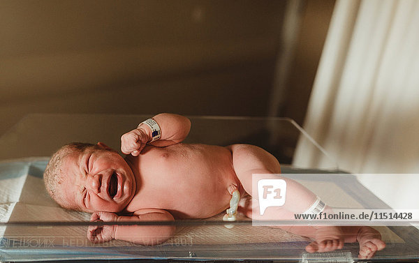 Nacktes  weinendes neugeborenes Mädchen liegt auf einer Krankenhaus-Gewichtswaage