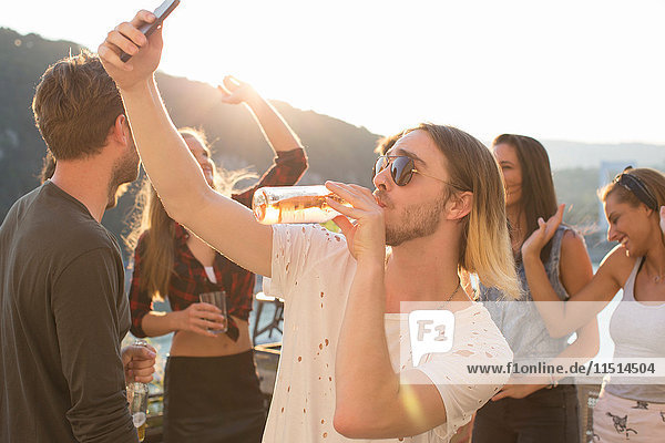 Young man taking selfie drinking beer at waterfront roof terrace party  Budapest  Hungary