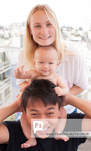 Portrait of parents with baby son on shoulders in front of window