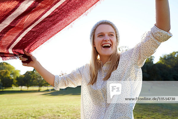 Young woman shaking picnic blanket in park