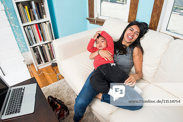 Frau mit Kleinkind Sohn auf Schoß lachend auf Sofa