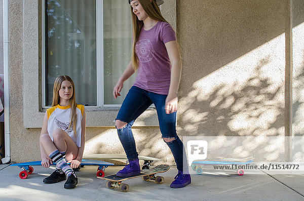 Zwei jugendliche Skateboarder-Schwestern üben auf der Veranda.