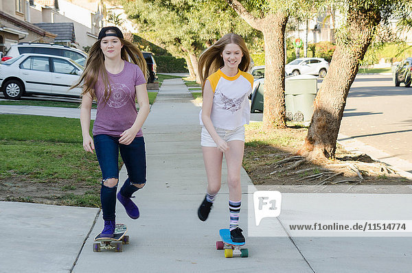 Zwei jugendliche Skateboardfahrer-Schwestern skateboarden auf dem Bürgersteig