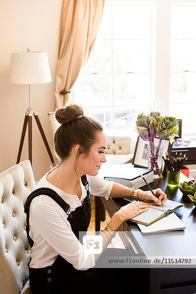 Weibliche Mode- und Lifestyle-Bloggerin schreibt am Schreibtisch in einem Notizbuch