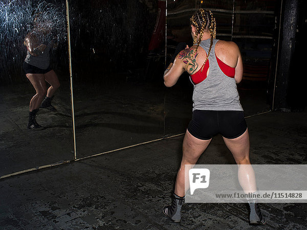 Rear view of female boxer sparring looking in gym wall mirror