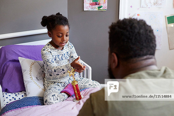 Father talking to young girl on bed with trophy