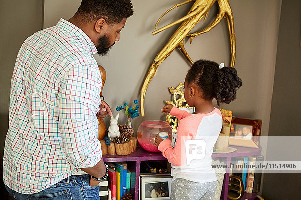 Father watching daughter feed fish in goldfish bowl