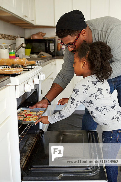 Father and daughter putting unbaked cookies in oven