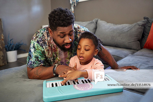 Girl lying on sofa with father playing toy keyboard