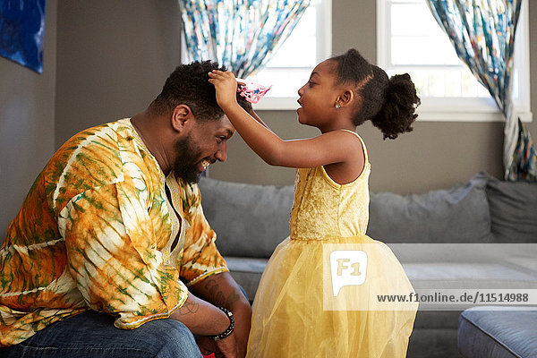 Girl in princess costume putting tiara on father in living room