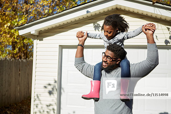Mature man carrying daughter on shoulders by residential garage