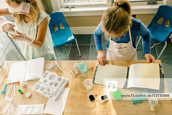 Draufsicht auf zwei Mädchen  die ein wissenschaftliches Experiment durchführen und Anweisungen des Chemie-Sets lesen