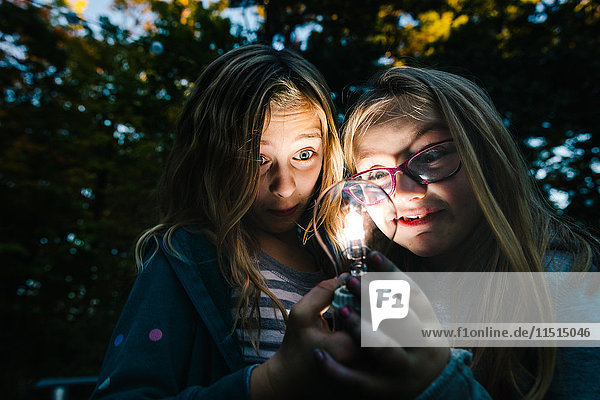 Zwei Mädchen  die in der Abenddämmerung im Garten eine beleuchtete Glühbirne halten und anstarren