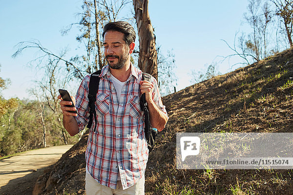 Mittelgroßer erwachsener Mann beim Wandern  Blick auf Smartphone