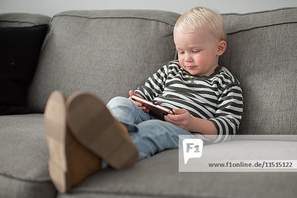 Junge sitzt auf dem Sofa und schaut auf ein Smartphone