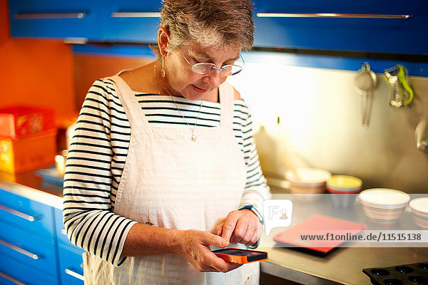 Senior woman in kitchen  using smartphone